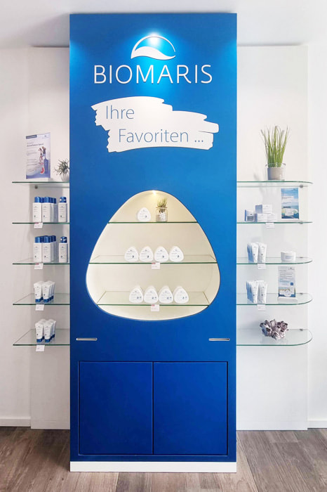 Präsentationswand in Blau mit BIOMARIS Favourites Produkten und Glasregalen mit Pflegeprodukten