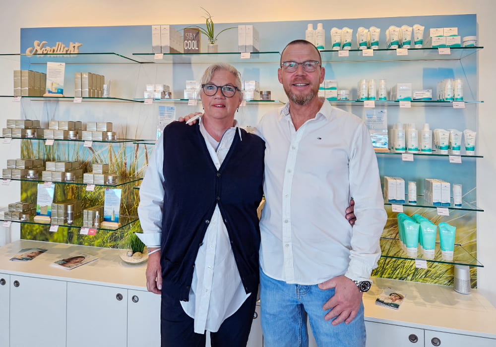 Biomaris Shop Westerland Ein Shop-Betreiber und eine Mitarbeiterin stehen lächelnd vor einem Verkaufsregal mit Biomaris-Produkten im modern gestalteten Laden.