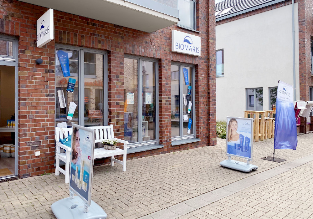 Außenansicht des BIOMARIS-Shops in Heiligenhafen mit roten Ziegeln, davor Werbetafeln, Fahne und Sitzbank