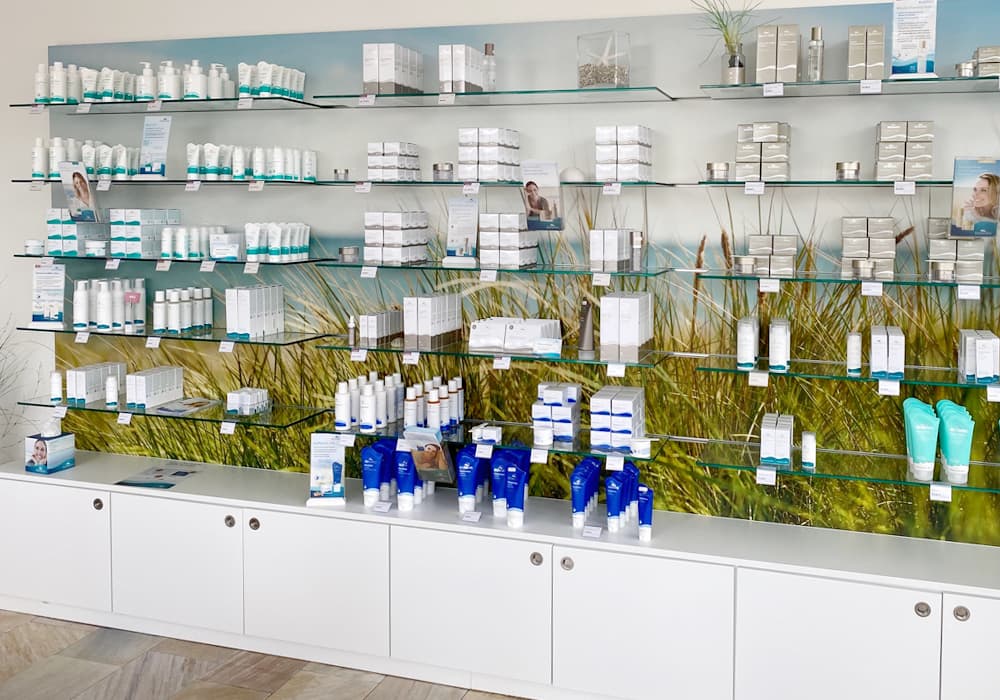 BIOMARIS Verkaufsregal mit Pflegeprodukten auf Glasböden vor Wandbild mit Dünenlandschaft