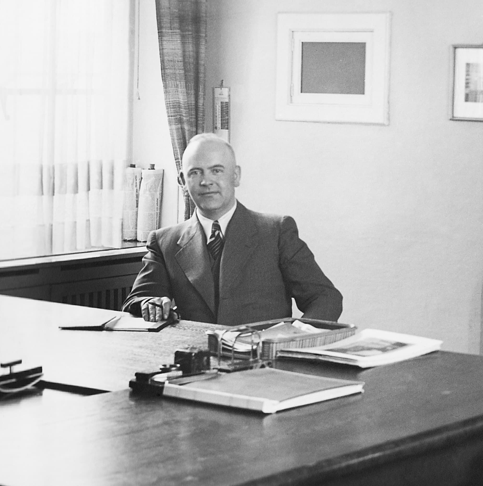 Walter Brachmann Schwarz-weiß-Porträt von Walter Brachmann, sitzend im Anzug an einem Schreibtisch in einem schlicht eingerichteten Büro.